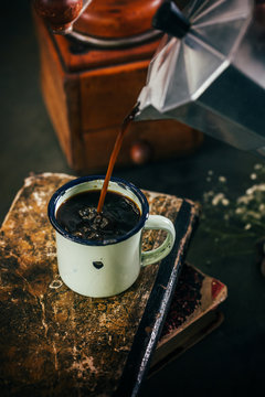 Poring hot coffee in an enamel cup with steam on dark mood