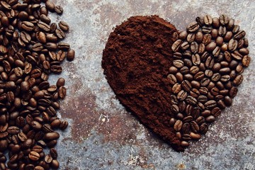 Coffee beans and ground coffee laid  out as a heart shape. Coffee cups and coffee beans isolated on vintage backgrond
