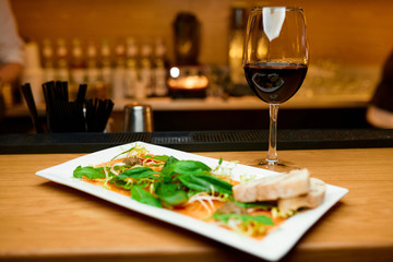 salmon carpaccio on a white plate with a glass of red wine