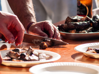 Unrecognizable person cutting meat with a knife and placing it on a paper plate in the street at a popular party in a village in Spain