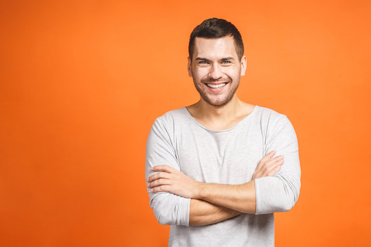 Casually Handsome. Confident Young Handsome Man Keeping Arms Crossed And Smiling While Standing Against Orange Background.