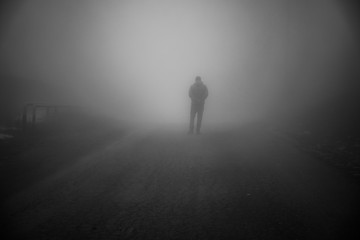 Man walking away on misty road. Man standing alone on rural foggy and misty asphalt road. - Powered by Adobe