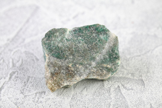 Natural rock specimens - green listvenite, listwanite mineral from Berezovsk, Ural, Russia on white cement background.