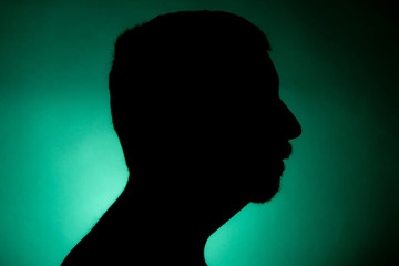 Cleanly defined silhouette of a male person turned to the left against a green background with a spotlight and bright area right behind the bust. Studio shot with strong explicit colour background.