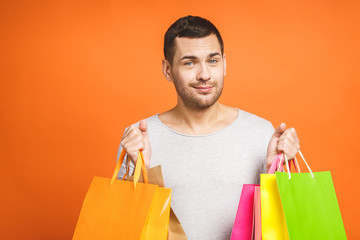 It's shopping time! Happy young man with colorful paper bags isolated on orange background.