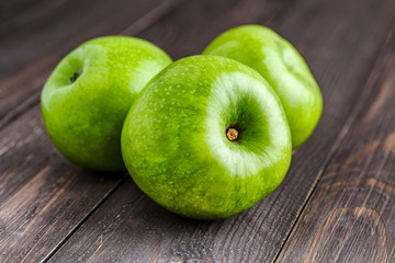 Ripe green apples and apple slices on old wooden background.