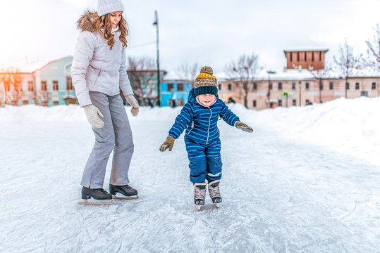 Young woman mom skates with her young son, a boy of 3-5 years. In the winter in the city on the rink. The first lesson and support of the parent in sports in nature.