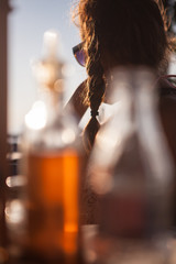 A teenager sits outside in a restaurant and looks into the sunset. In the foreground unfocused vinegar and oil. warm colours.