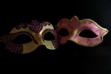 Two Venetian masks with gold, pink and purple color on black background