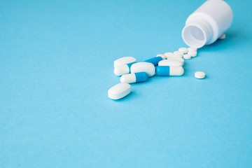 Close up pills spilling out of pill bottle on blue background. Medicine, medical insurance or pharmacy concept