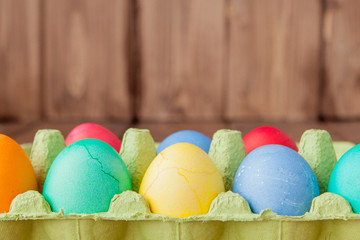 Colorful Easter eggs in box on wooden background with copy space