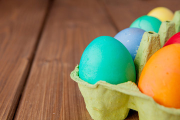 Colorful Easter eggs in box on wooden background with copy space