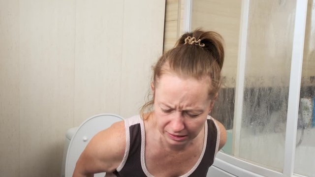 Girl sitting on the toilet contorts face from unpleasant odor of feces.