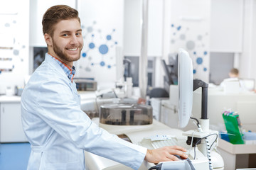 Handsome young male laboratory technician operating computerized analyzing machine