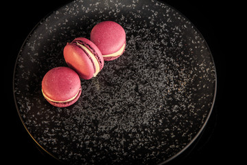 closeup three purple macaroons served on black plate