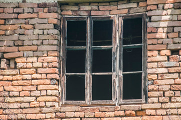 Old weathered aged wooden frame window on red brick wall of abandoned country house closeup