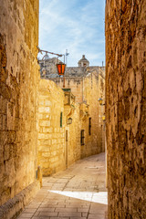 Sunny midday beautiful narrow typical limestone street with lanterns in Mdina - Citta Vecchia or Citta Notabile in Malta