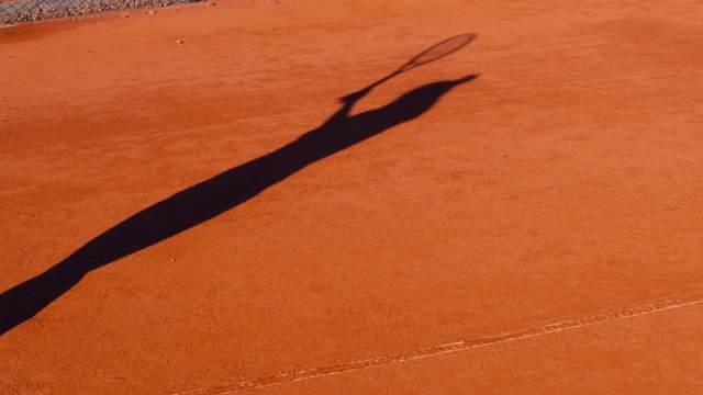 Shadow of tennis player serving tennis ball on clay court. Slow motion 75fps