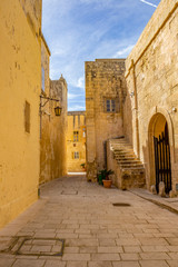 Fototapeta na wymiar Sunny midday beautiful narrow typical limestone street with a lantern in Mdina - Citta Vecchia or Citta Notabile in Malta
