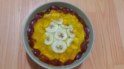 Creamy tasty sweet custard with banana pieces on surface inbowl on wooden floor