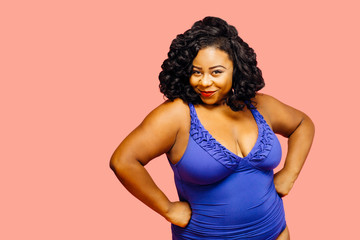 Portrait of a beautiful plus size model in a bathing suit with arms on waist, isolated on pink