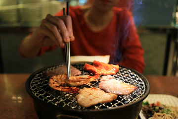 Woman enjoying grilling barbecue on mesh grill of charcoal fire. Korean or japanese traditional roast food style barbecue.