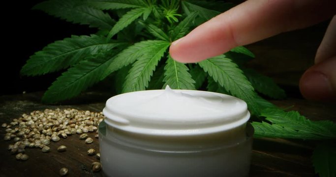 Slow motion close up of a female hand dosing a cream with biological and ecological hemp plant herbal pharmaceutical cbd oil from a jar.