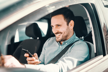 Close up of smiling bearded man using smart phone for writing or reading message with hand on the...