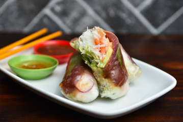 Traditional Vietnamese cuisine dish - fresh spring rolls wrapped in transparent rice paper with tuna, avocado, vermicelli, carrot inside served with spicy sauces 