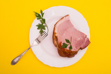 A large piece of fresh pork ham on a plate on a yellow background