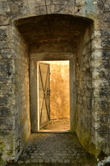 geöffnete antike metalltüre durch die das licht hindurchscheint in alter steinmauer