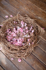Naklejka premium Cherry tree blossoming flowers in straw nest on brown wooden background. Easter background with a nest with sakura spring flowers. Rustic wooden background for easter. Pink sakura flowers in a nest