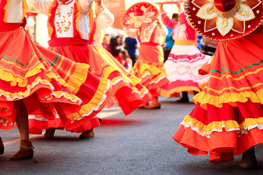 a group of mexican women dancing with bright handmade mexican dresses during mexican carnival