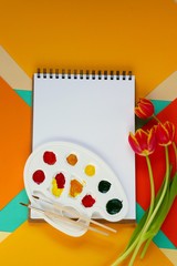 Spring Flat lay. album for drawing, a bouquet of red tulips flowers, paints on a geometrical  bright background.Spring mood. top view, copy space