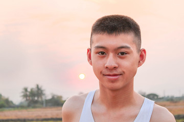 Asian teen boy standing smile at the field with sunset background in evening.