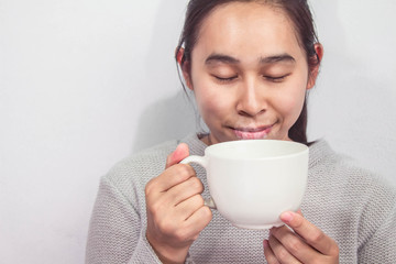 An Asian woman is sitting and smelling coffee with happiness in the room. Happy time concept.