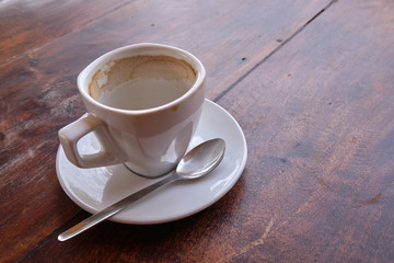 Empty white cup of coffee in saucer with spoon, on old wood marked table.  Stain from the coffee visible inside cup.