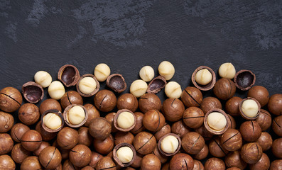 Obraz premium Shelled and unshelled macadamia nuts on black table, with copy space. Top view.