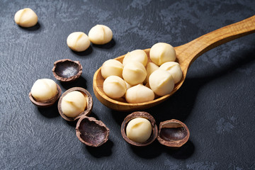 Shelled  macadamia nuts in wooden spoon on black table, close-up. Top view - obrazy, fototapety, plakaty