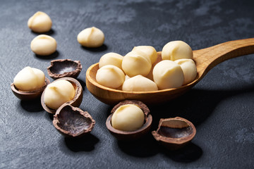 Shelled  macadamia nuts in wooden spoon on black table, close-up.