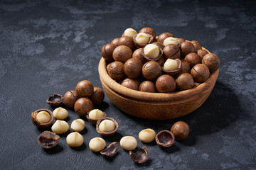 Organic macadamia nuts in wooden bowl on black background, close-up.