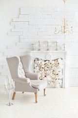 Elegant soft arm-chair near a fireplace. Luxury interior in white colors. Armchair with fabric upholstery