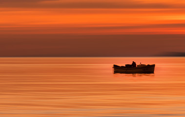 Boat With a Man on the Sea Water on the horizon against the background of a fiery red sunset/sunrise