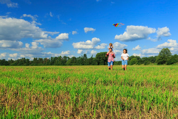 Mother, father and daughter are flying a kite in the field. Front view, copy space.