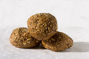 Several round dark colored buns with varios seeds on a light background. Close up. Buns for a breakfast, filling, dessert