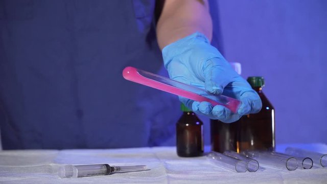 Lab technician with sterile gloves will mix red liquid in test tube for analysis