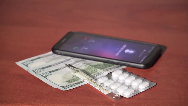 Woman finger rejected call of black cell phone which was lying beside money and pills. Close up