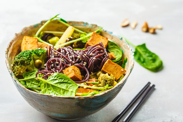 Vegan black rice noodles with tofu and vegetables, white background.