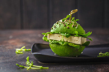 Vegan avocado tofu burger on black dish. Healthy detox food, plant based food concept.