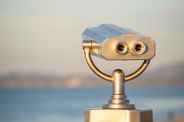 Public binocular on sea shore, close up. Coin operated binocular viewer on blurred background of sunset and sea